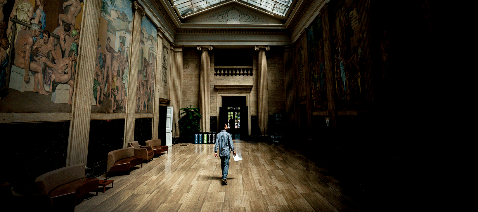 Man holding paper in one hand walking through a darkened atrium